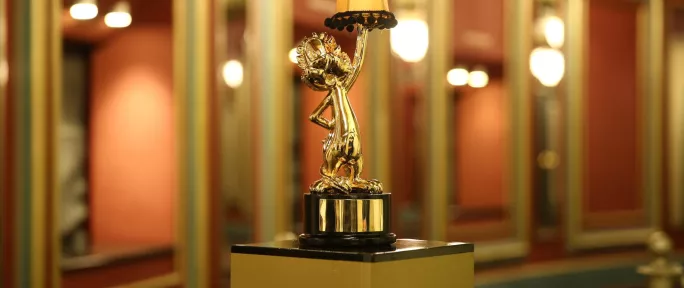 A golden Loekie Award trophy featuring a stylized dog holding a small lampshade with the word "Ster" on it, placed on a black and gold pedestal indoors with a blurred background and warm lighting.