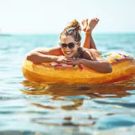 An online Neckermann ad of a smiling woman in sunglasses on a colorful inflatable in the ocean. Text reads in Dutch ‘For elke vacation fan, there is Neckermann’.