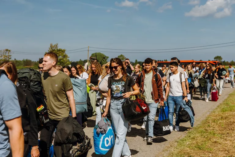 A large group of smiling Springbok employees walks along a rural path, carrying bags and backpacks. The sky is clear and sunny, creating a cheerful atmosphere.