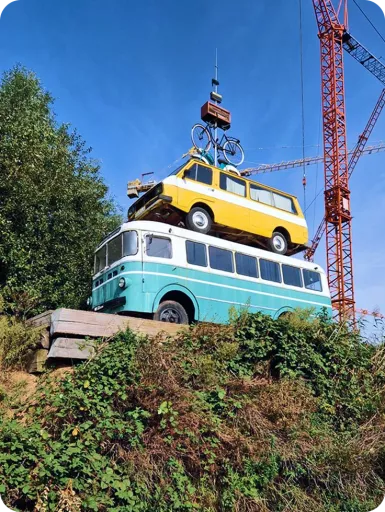 Springbok's Time To Make Sense 2025 Summit at the Verbeken Foundation contemporary art museum. Art installation with a blue vintage bus supports a yellow bus on top, with a bike perched above, surrounded by greenery and a crane in the background.